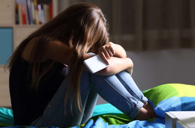 A young girl sitting alone on her bed, holding her phone