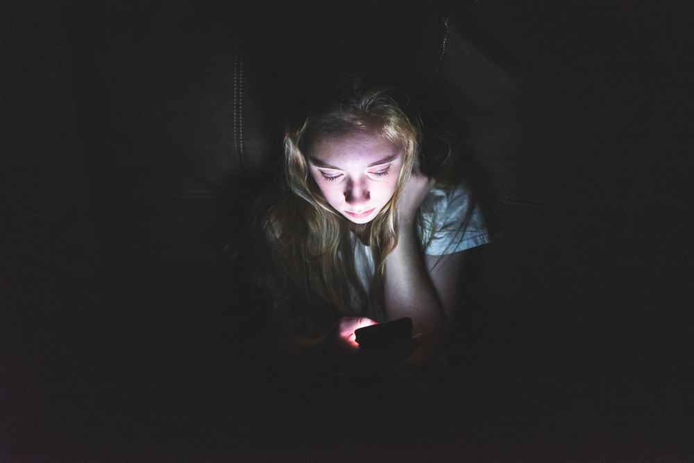 A young girl looking at her phone screen in the dark