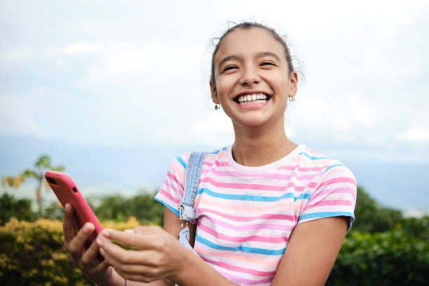 A smiling young girl outdoors holding her phone