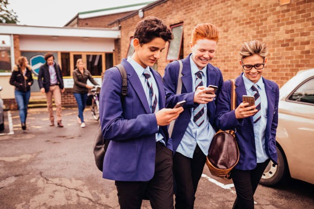 A group of schoolboys laughing together while looking at their phones